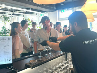 Abbildung von Azubis an einer Bar, ein Barkeeper macht einen Cocktail.