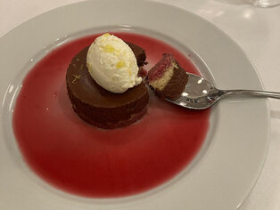 Abbildung einer Dessertkomposition mit Schokokuchen, Eis, roter Sauce und Löffel auf weißem Teller.