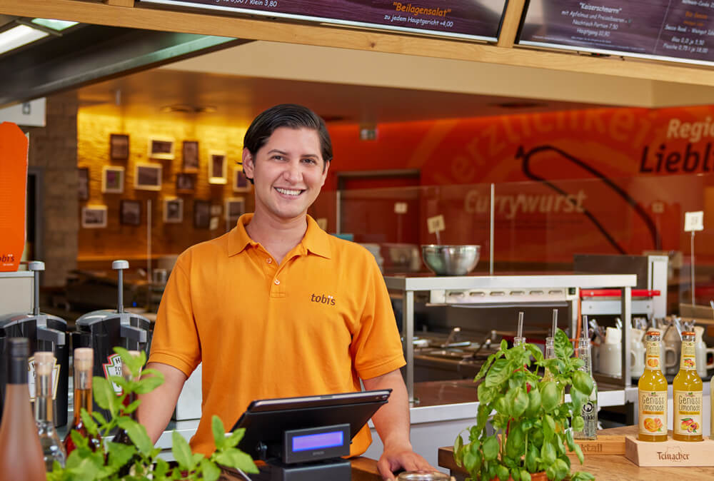 Abbildung eines Mannes in Arbeitskleidung an einer Theke eines Restaurants.