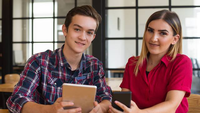 Abbildung von zwei Personen mit Tablet und Smartphone an einem Tisch.