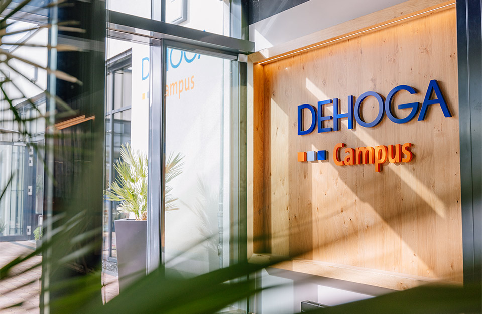 Abbildung einer Wand mit Schriftzug „DEHOGA Campus“ und Glasfront.