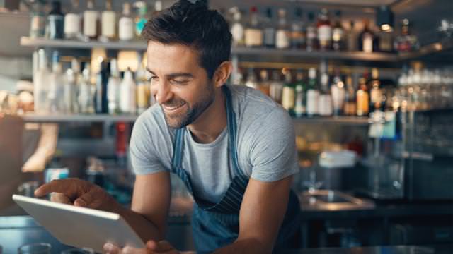 Abbildung eines Mannes hinter einer Bar mit Tablet, im Hintergrund Regale mit Flaschen und Gläsern.