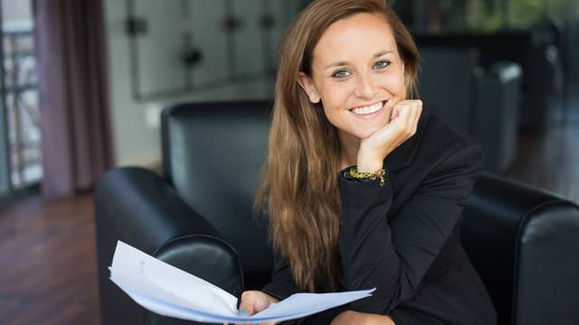 Abbildung einer Frau auf einem Stuhl mit Papieren in der Hand.