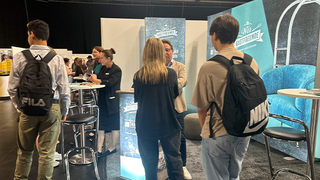 Abbildung von mehreren Personen auf einer Messe im Gespräch bei Stehtischen.