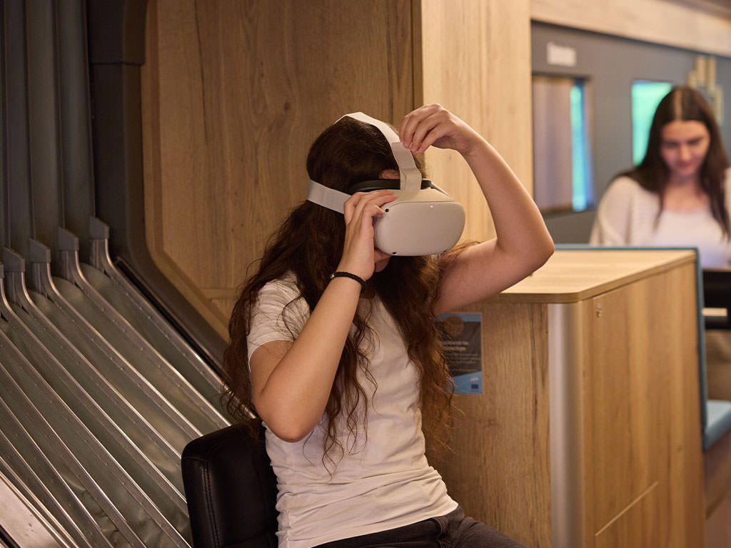 Abbildung einer Person mit Virtual-Reality-Brille, sitzend auf einem Stuhl.