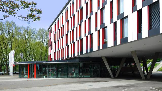 Abbildung eines modernen Gebäudes mit rot-weißer Fassade und schrägen Stützen.