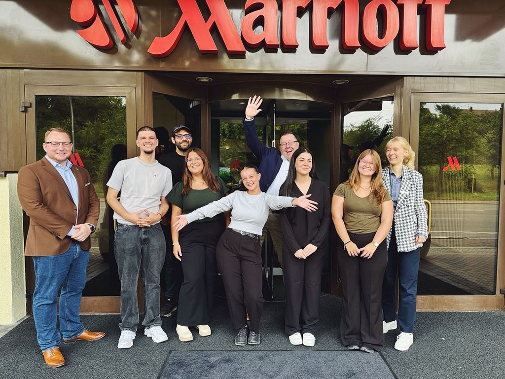 Abbildung von neun Personen vor dem Eingang eines Marriott Hotels, posierend unter dem gut sichtbaren Logo.