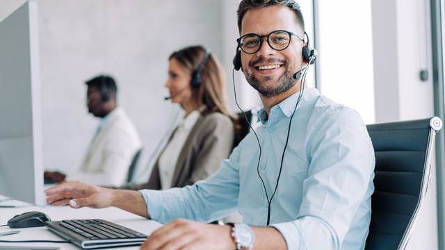 Abbildung von drei Personen mit Headsets an Schreibtischen in einem Büro.